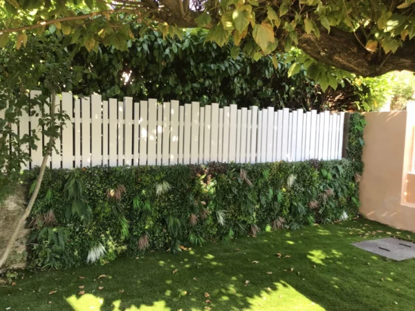 Clôture blanche à lames ajourées installée sur un muret orné de plantes végétales