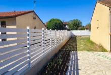 Clôture blanche à lames horizontales ajourées installée sur un muret entre deux maisons