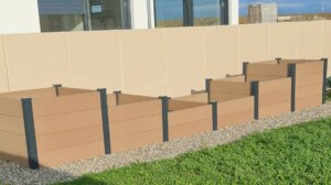Carré potager en composite divisé en 6 cases où poussent des fraisiers, du basilic et des laitues frisées.