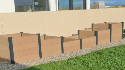 Carré potager en composite divisé en 6 cases où poussent des fraisiers, du basilic et des laitues frisées.