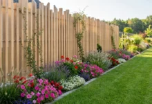 clôture effet bois à lames verticales installée sur un petit muret garni de fleurs