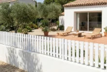 clôture à lames verticales ajourées blanche posée sur un muret enduit blanc dans un jardin de style bali