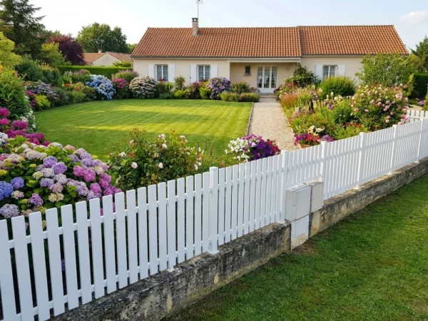clôture ajourée posée sur un muret ancien autour d'un jardin fleuri