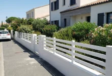 clôture blanche ajourée posée sur un muret entre piliers béton crépis
