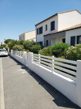 clôture blanche ajourée posée sur un muret entre piliers béton crépis