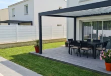 clôture occultante blanche sur un muret habillée de pierre à côté d'une terrasse en bois et d'une pergola