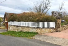 clôture ajourée blanche à lames verticales posée sur un muret en pierre