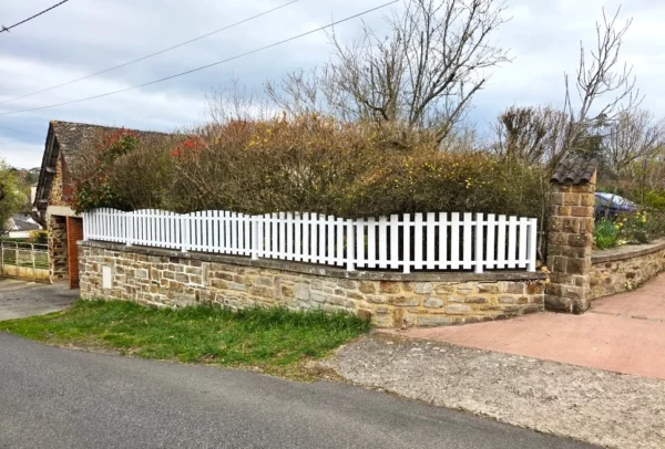 clôture ajourée blanche à lames verticales posée sur un muret en pierre
