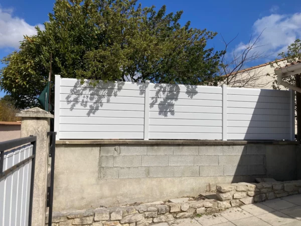 Clôture persienne blanche posée au dessus d'un muret en parpaings