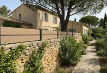 Clôture beige posée sur un muret en pierres traditionnelles
