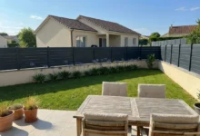 clôture ajourée grise foncée, fixée sur un muret enduit, délimitant une maison récente.