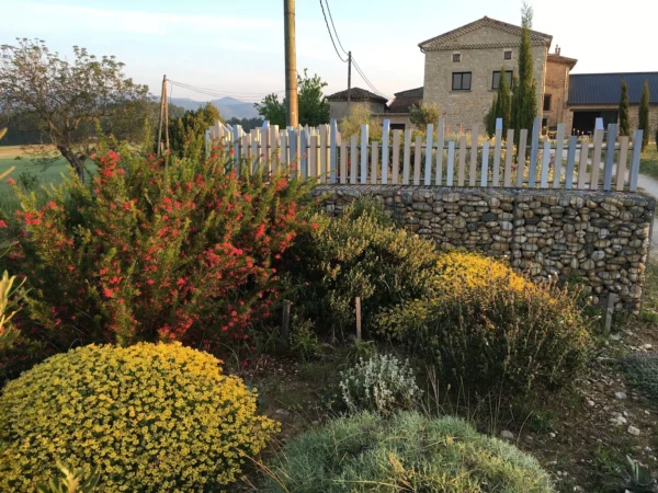 clôture PVC ajourée Abysse posée sur gabion en pierre, dans un jardin paysager devant une maison en pierre