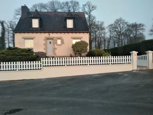 clôture ajourée à lames verticales installée sur un petit muret en pente