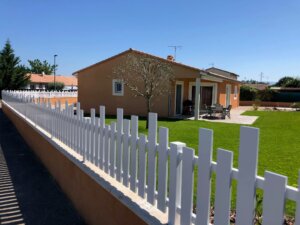Clôture en pvc blanc ajourée installée avec des lames verticales en coupe irrégulière pour aménager votre jardin