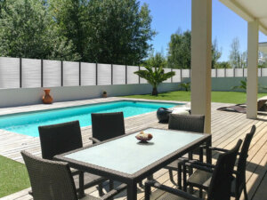 Clôture en pvc blanc ajourée sur muret avec des poteaux aluminium gris anthracite et des lames horizontales de 50 mm