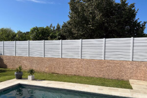 Clôture en pvc blanc ajourée avec des poteaux pvc blanc installée sur muret en bord de piscine