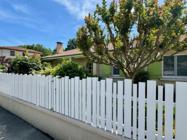 Clôture en pvc blanc ajourée sur muret installée avec une variation subtile des largeurs de lames