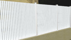 Clôture en pvc blanc ajourée sur muret installée avec des lames verticales en coupe droite