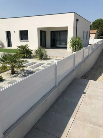 clôture blanche pleine posée sur un petit soubassement autour d'une maison à toit plat