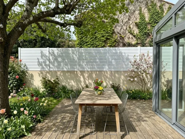clôture blanche posée sur un muret crépis ton pierre prés d'un terrasse en bois et d'une véranda