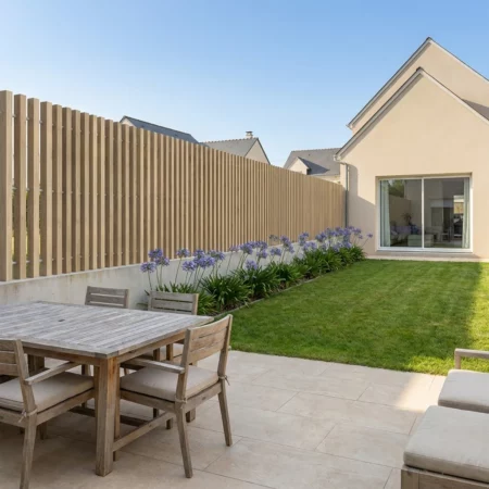 clôture imitation bois à lames verticales ajourées sur un muret dans lotissement de maisons neuves