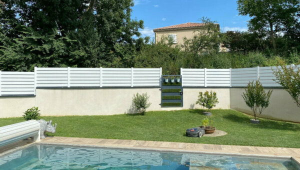 Clôture en pvc blanc brise-vue sur muret installée avec des lames biseautées au bord d'une piscine