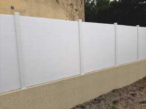 Clôture en pvc blanc brise-vue sur muret installée avec des lames imbriquées les unes aux autres