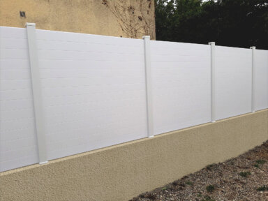 Clôture en pvc blanc brise-vue sur muret installée avec des lames imbriquées les unes aux autres