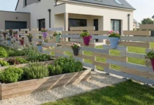 clôture patchwork ajourée avec des pots de fleurs intégrés prés d'un potager