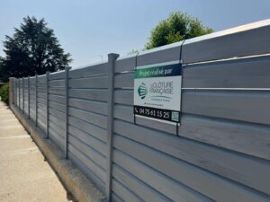 Vue d'une clôture Cerbère en PVC gris, à lames inclinées pour préserver des regards extérieurs tout en laissant passer l'air et la lumière.