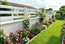 Clôture ajourée en PVC blanc posée sur muret avec un parterre de fleurs