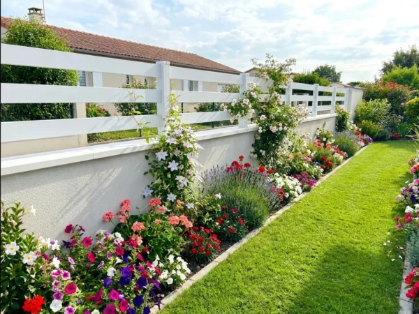 Clôture ajourée en PVC blanc posée sur muret avec un parterre de fleurs