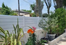 Clôture à lames biseautées installée sur un joli muret enduit et fleuri