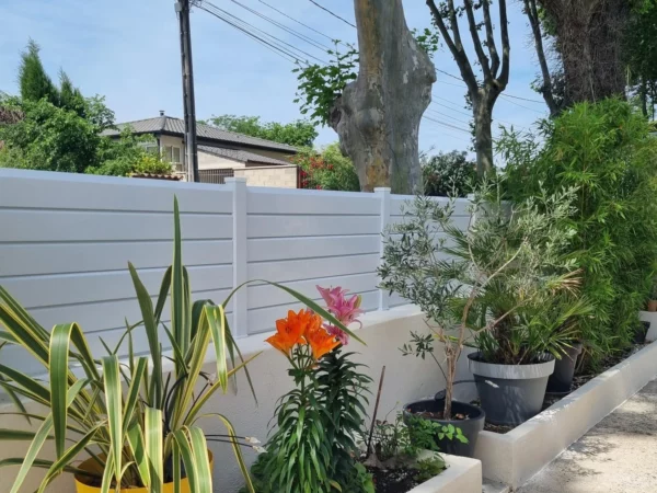 Clôture à lames biseautées installée sur un joli muret enduit et fleuri