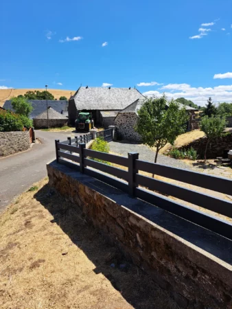 Clôture d'une petite hauteur de couleur gris foncé posée sur un muret en pente