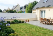 Clôture à lames blanches et pleines posée dans le jardin d'une maison au toit en ardoise