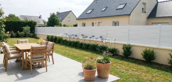Clôture bise vue installée sur un muret avec des fleurs de type agapanthes
