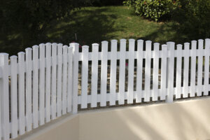 Clôture en pvc blanc ajourée installée avec des lames verticales en coupe bombée pour aménager votre jardin
