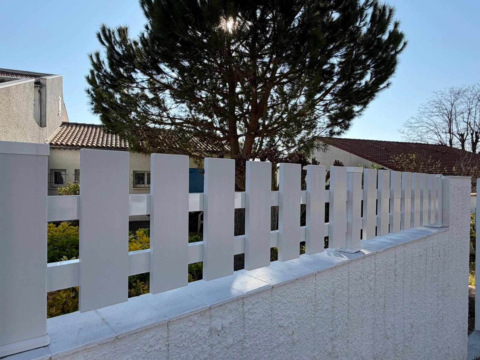 clôture blanche à lames verticales ajourées d'une petite hauteur sur un muret crépis