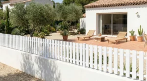 clôture à lames verticales ajourées blanche posée sur un muret enduit blanc dans un jardin de style bali