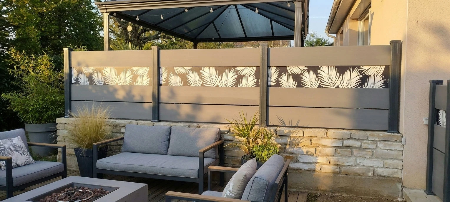 clôture grise à lames larges avec une impression personnalisée installée sur un muret en pierres