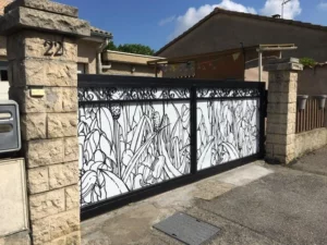 Portail coulissant décoratif noir et blanc avec motifs floraux, installé entre deux piliers en pierre à l’entrée d’une maison